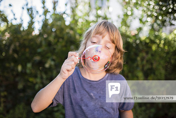 Blond little boy blowing soap bubble