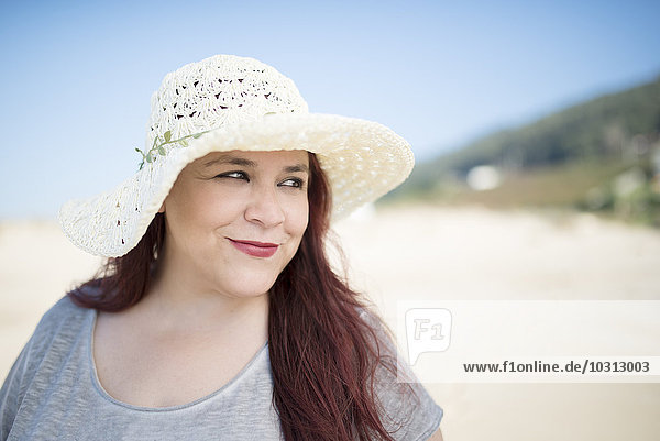 Porträt einer lächelnden Frau mit Hut am Strand