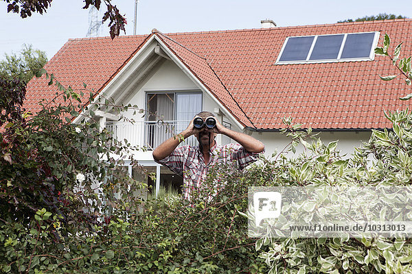 Mann schaut durchs Fernglas über Hecke