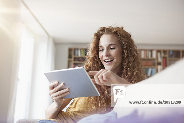Smiling woman at home sitting on couch using digital tablet