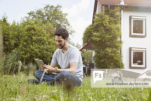 Mann im Garten sitzend mit digitalem Tablett