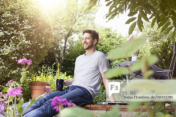 Smiling man sitting in garden with cup of coffee