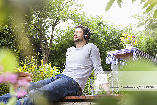 Entspannter Mann im Garten sitzend mit Kopfhörer