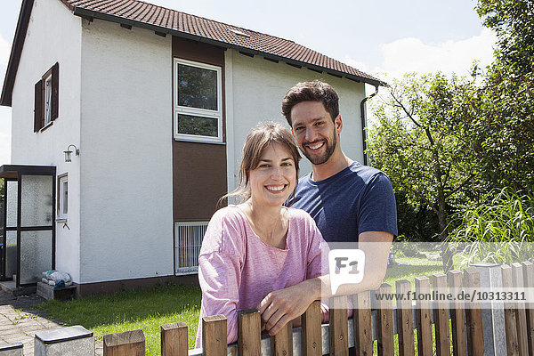 Porträt des lächelnden Paares im Garten vor dem Wohnhaus