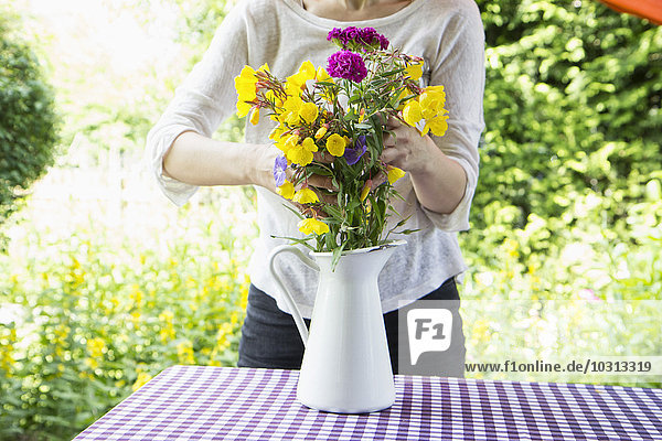 Frau arrangiert Blumenstrauß auf Gartentisch