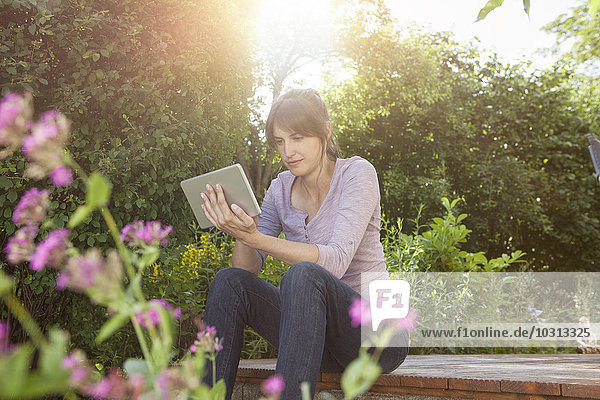 Frau im Garten sitzend mit digitalem Tablett
