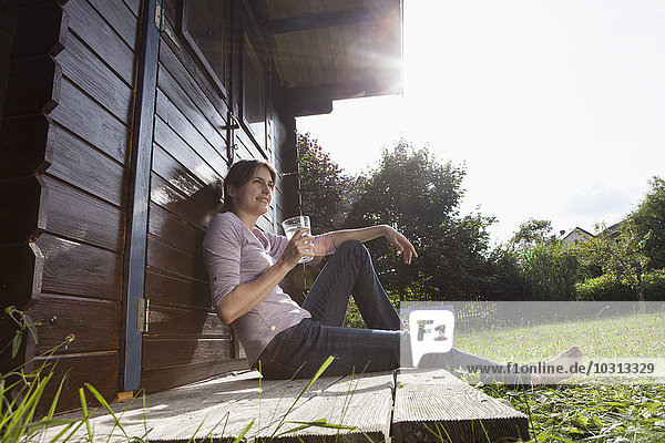 Lächelnde Frau sitzend im Gartenhaus mit einem Glas Wasser