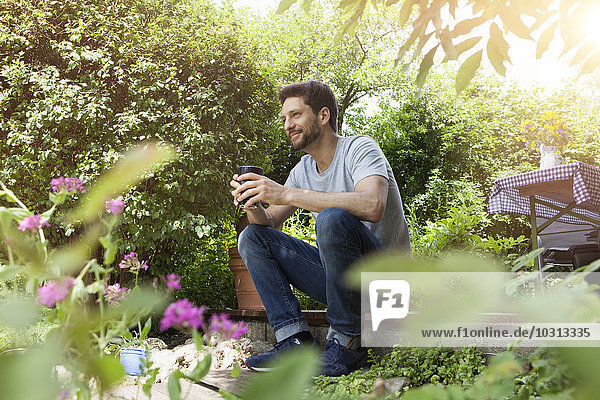 Smiling man sitting in garden with cup of coffee