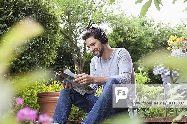 Entspannter Mann im Garten sitzend mit Kopfhörer und Magazin