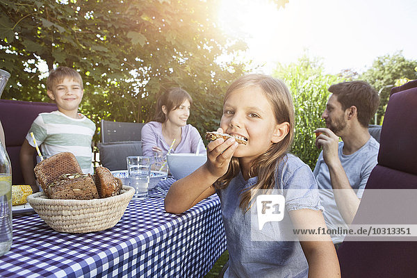 Mädchen beim Brotessen mit der Familie am Gartentisch