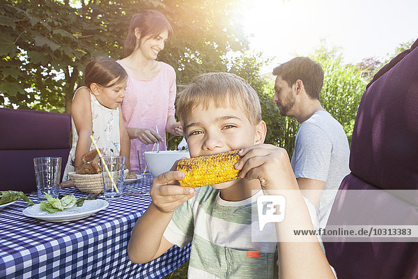 Junge beim Essen eines Maiskolbens auf einem Familiengrill im Garten