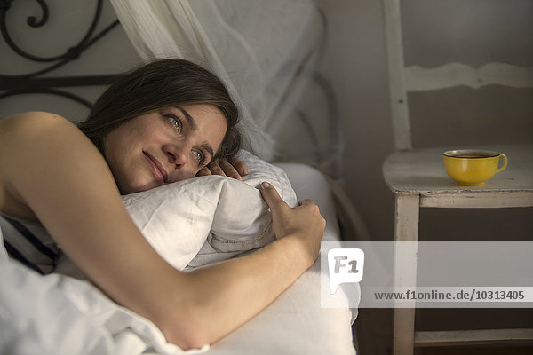 Junge Frau im Bett liegend  Kissen umarmend