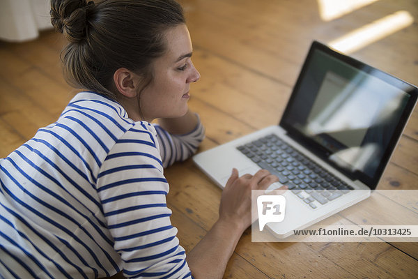 Junge Frau zu Hause auf Holzboden liegend  mit Laptop