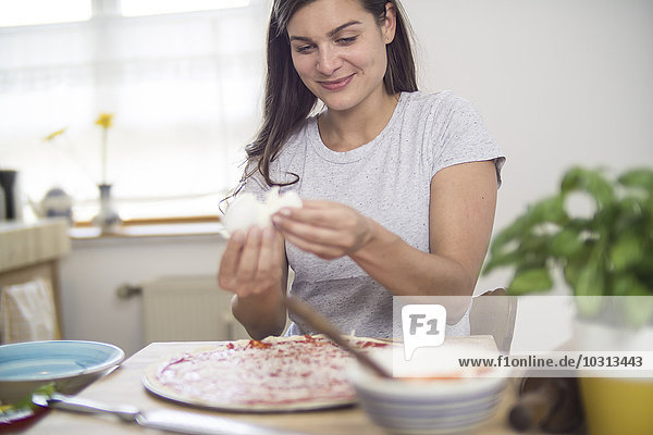 Young woman putting mozzarella cheese on pizza