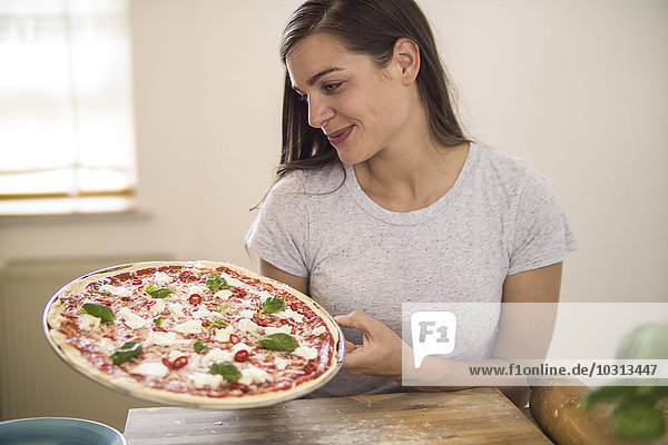 Young woman holding homemade pizza with mozzarella  chili peppers and basil