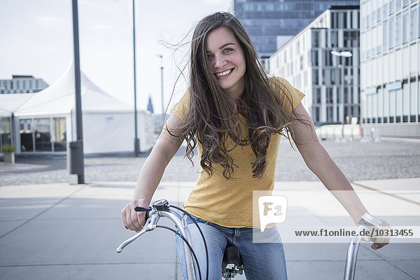 Deutschland  Köln  Porträt einer lächelnden jungen Frau mit blasenden Haaren auf dem Fahrrad