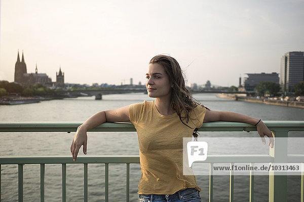 Deutschland  Köln  junge Frau steht in der Abenddämmerung auf der Rheinbrücke