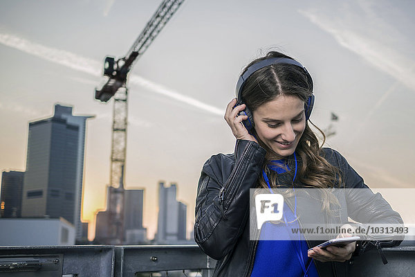 Deutschland  Frankfurt  lächelnde Frau  die Musik mit Kopfhörern hört und ihr Smartphone ansieht.