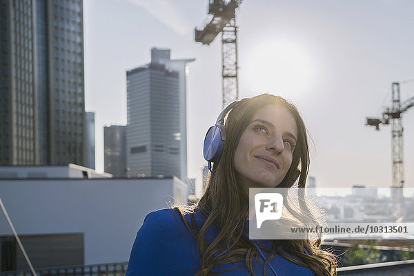 Deutschland  Frankfurt  Porträt einer lächelnden Frau  die Musik mit Kopfhörern im Gegenlicht hört.