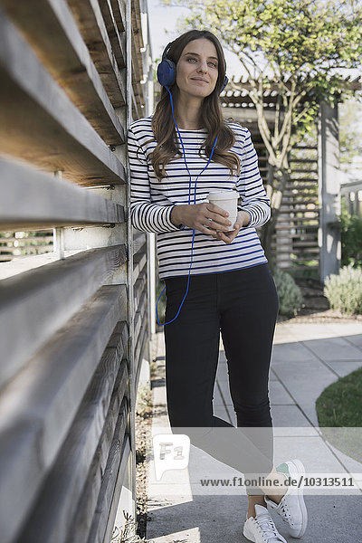 Portrait of smiling woman with coffee to go hearing music with headphones