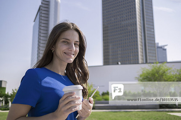 Deutschland  Frankfurt  Porträt einer lächelnden Frau mit Kaffee zum Mitnehmen und Mini-Tablette