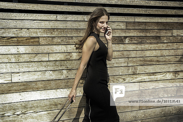 Porträt einer lächelnden Geschäftsfrau beim Telefonieren mit dem Smartphone vor der Holzwand