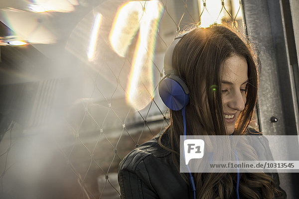 Deutschland  Frankfurt  lächelnde Frau hört Musik mit Kopfhörern im Gegenlicht