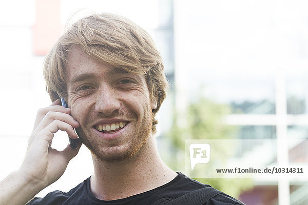 Porträt eines lächelnden jungen Mannes beim Telefonieren mit dem Smartphone