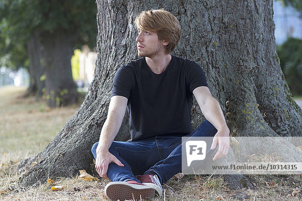 Pensive young man sitting in front of tree trunk