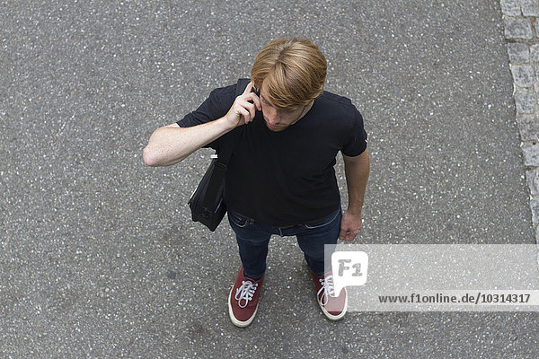 Portrait eines jungen Mannes  der auf einer Straße steht und mit einem Smartphone telefoniert.