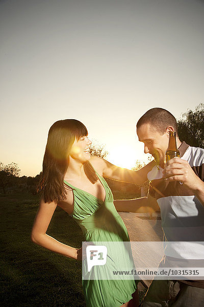 Fröhliches junges Paar tanzt mit Bierflasche bei Sonnenuntergang