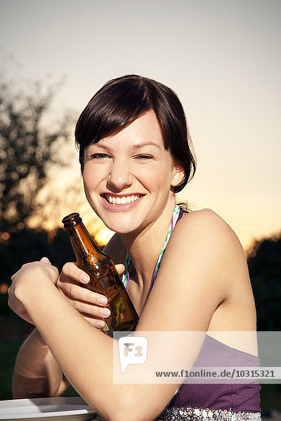 Glückliche junge Frau  die bei Sonnenuntergang ein Bier trinkt.
