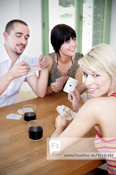 Junge Frau zeigt Pik-Ass  während ihre Freunde Karten spielen