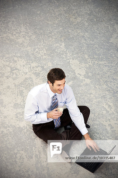 Smiling businessman sitting on floor using laptop