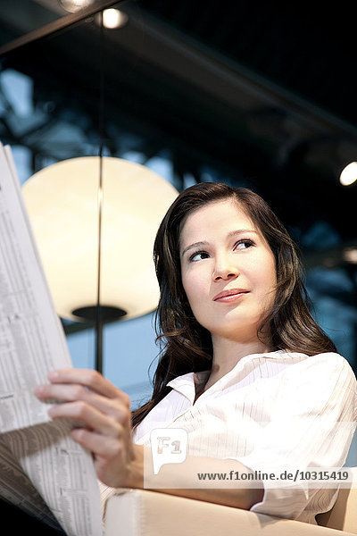 Young businesswoman sitting in armchair reading newspaper