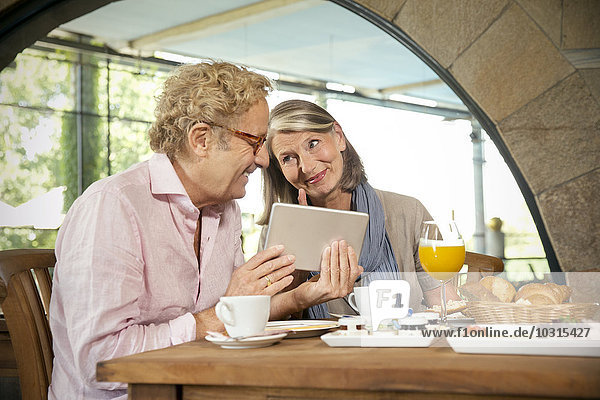 Smiling senior couple with digital tablet having breakfast in a cafe