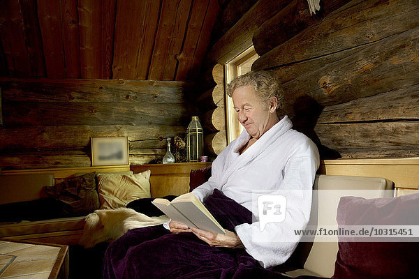 Smiling senior man sitting on bench in bathrobe reading a book