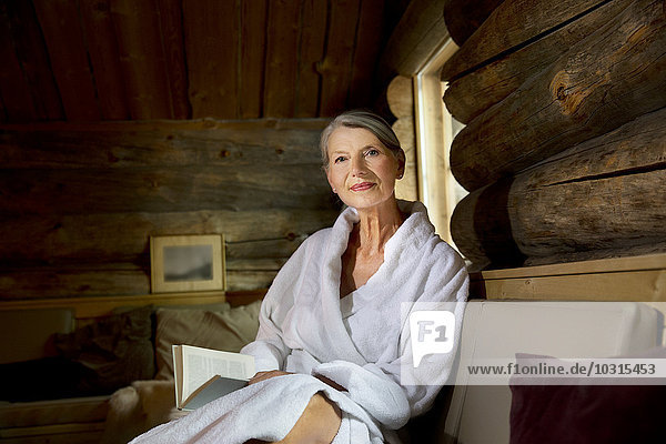 Smiling senior woman sitting on bench in bathrobe with a book