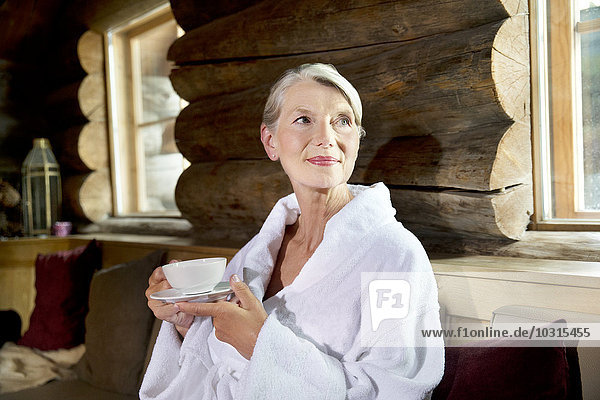 Smiling senior woman in bathrobe drinking tea