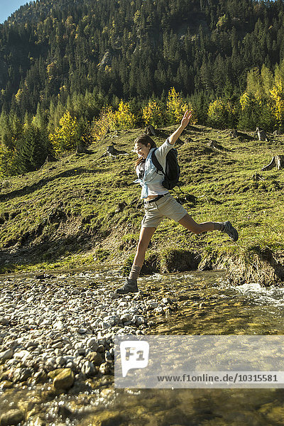 Österreich  Tirol  Tannheimer Tal  junge Wanderin beim Überqueren des Wassers