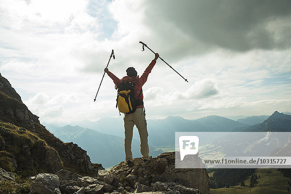Austria  Tyrol  Tannheimer Tal  young woman with hiking poles cheering on mountain top