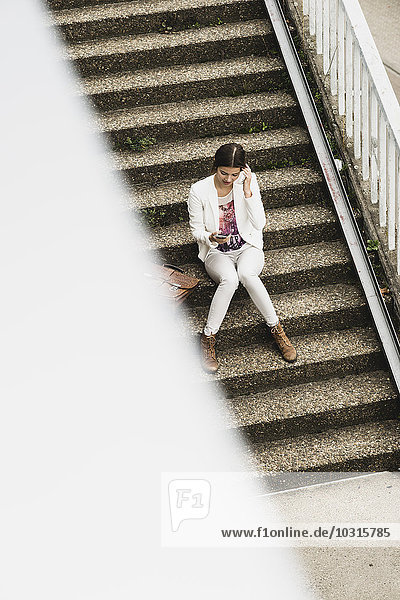 Junge Frau auf einer Treppe sitzend mit ihrem Smartphone  erhöhte Ansicht