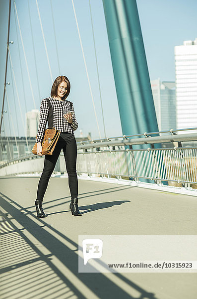 Deutschland  Frankfurt  junge Geschäftsfrau auf Brücke stehend mit Handy