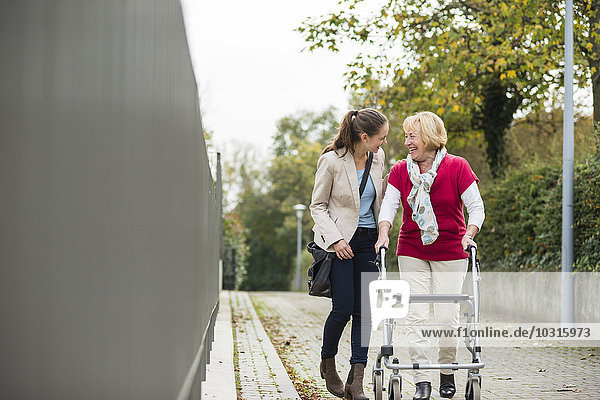 Adult granddaughter assisting her grandmother walking with wheeled walker