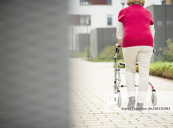 Senior woman walking with wheeled walker  back view