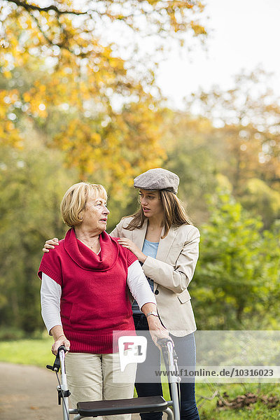 Senior woman and her caring adult granddaughter walking together in autumnal park