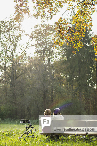 Senior woman and granddaughter sitting on a park bench  back view
