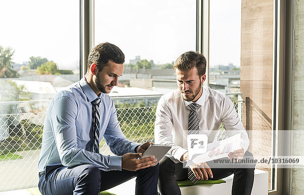 Zwei junge Geschäftsleute auf der Suche nach Dokument und digitalem Tablett
