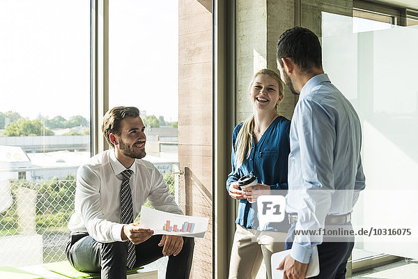Drei lächelnde junge Geschäftsleute diskutieren Dokument