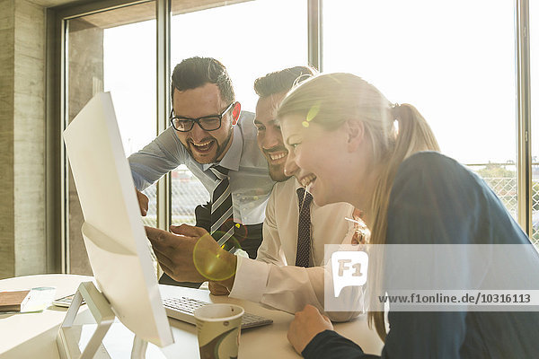Drei lachende junge Geschäftsleute im Konferenzraum mit Blick auf den Monitor